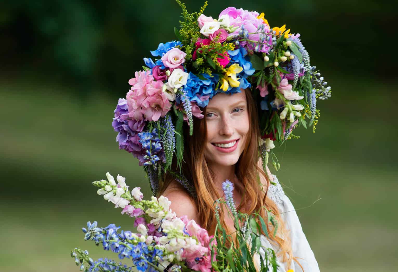 kobieta modelka z dlugimi wlosami w wianku z kwiatow i ziol i kolorowym bukietem na lace
