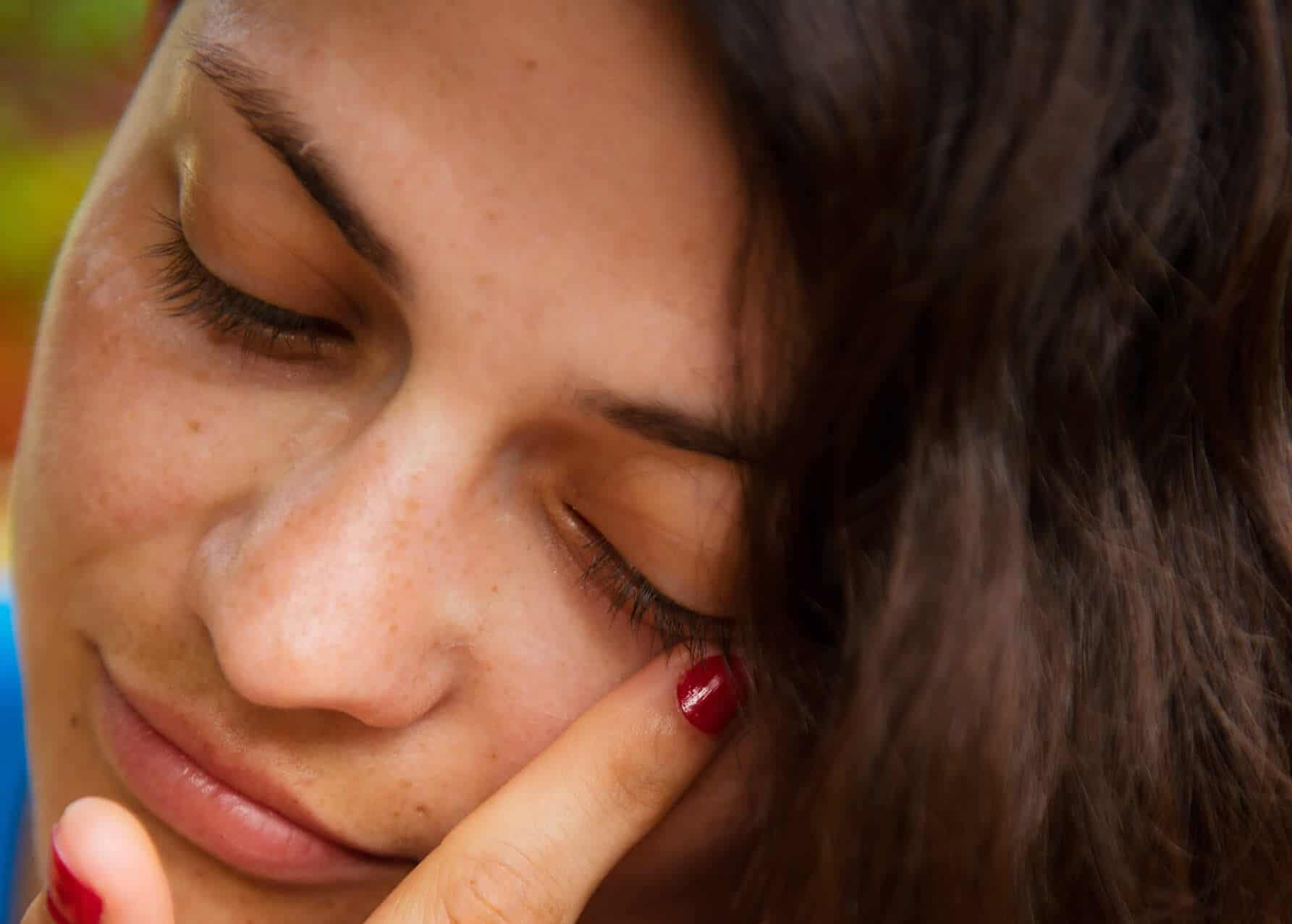 kobieta brunetka zamyslona z opuszczonymi powiekami dotyka dlonia twarzy