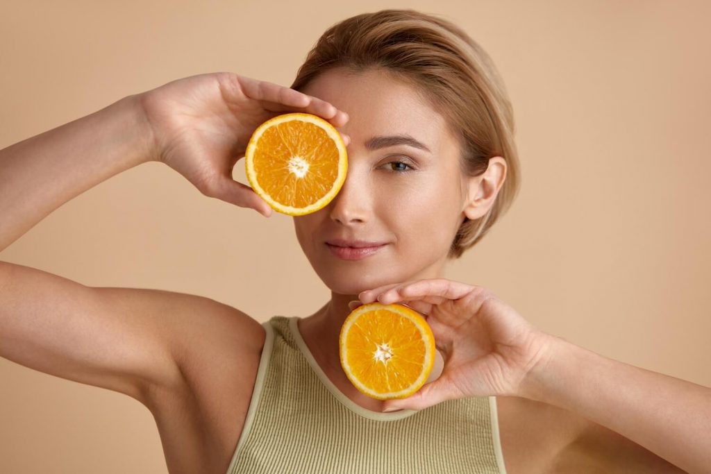 uśmiechnięta kobieta trzymająca przekrojone połówki pomarańczy